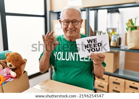 Senior volunteer man holding we need you banner doing ok sign with fingers, smiling friendly gesturing excellent symbol 