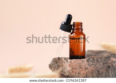 Cosmetic amber glass dropper bottle on wooden podium with pampas grass in soft focus. Oil, serum, fruit peeling. Natural beauty product presentation, pastel background. Front view. Mockup concept 