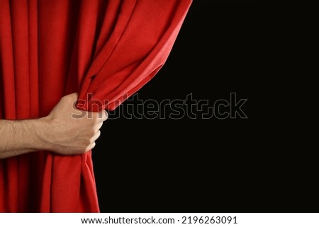 Man opening red front curtains on black background, closeup. Space for text Royalty-Free Stock Photo #2196263091