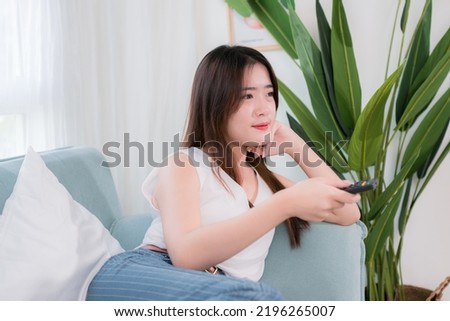 Asian woman use remote control for watching tv her enjoy and fun sitting near sofa in living room at home