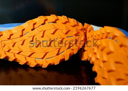 The soles of the two shoes were placed sideways on the black floor, Orange tread soles for trail running. The sole is very thick for wading on smooth roads and muddy roads. Royalty-Free Stock Photo #2196267677