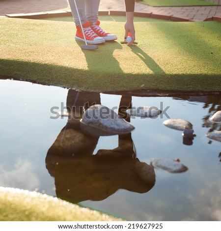 Detail of young woman playing mini/adventure golf on a beautiful sunny summer day (reflection in water, photo was taken in warm evening light)