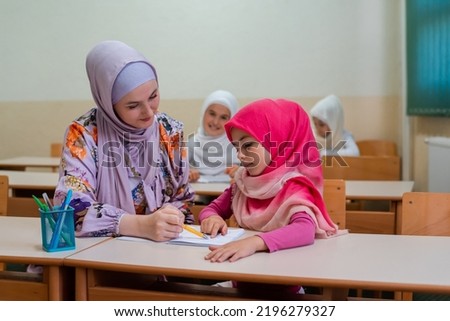Female hijab Muslim teacher helps student girl to finish the lesson durind the school class in the classroom.	