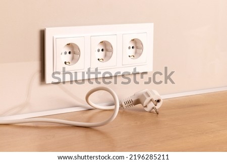 Power cord cable unplugged with group of white european electrical outlets on modern beige wall Royalty-Free Stock Photo #2196285211