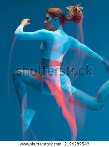 Sporty girl running in white tracksuit on blue background. Isolated fitness model in studio with motion blur effect.
