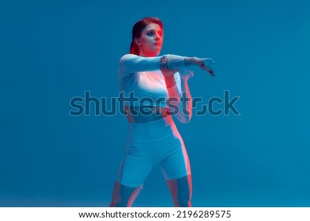 Beautiful girl in white tracksuit on blue background. Hand strike. Isolated fitness model in studio with motion blur effect. 