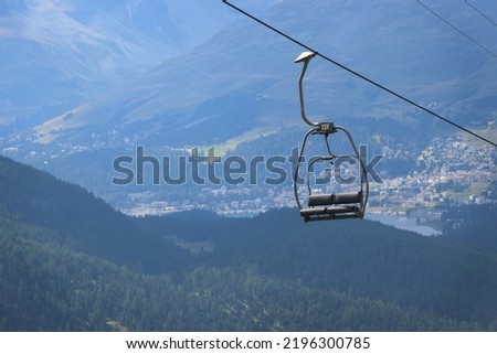 An empty chairlift on its way up. In the background is Saint Moritz, Switzerland. Royalty-Free Stock Photo #2196300785