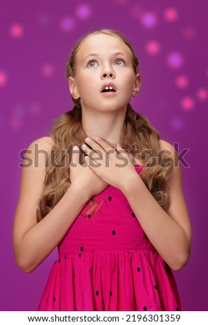 A cute blonde girl with pigtails wearing a red summer dress looks thoughtfully and with surprise up. Studio shot on a purple background. Children and emotions.