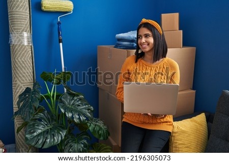 Young latin woman smiling confident using laptop at new home