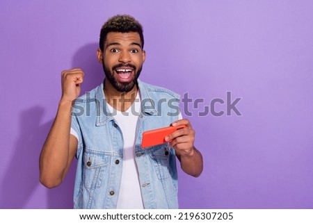 Photo of cute lucky guy dressed denim vest rising fist watching video modern device empty space isolated purple color background