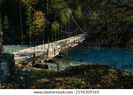 Beautiful, atmospheric shot of a wooden bridge over a mountain river for cars and people on a sunny autumn day. Impressive landscape of mountains, wooden bridge over the river