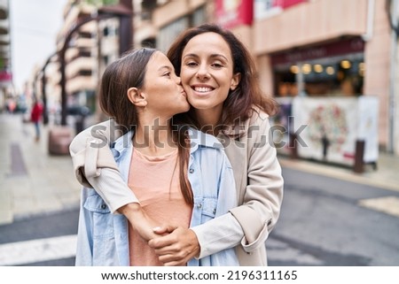 Woman and girl mother and daughter hugging each other and kissing at street