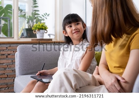Young Asian girl using digital tablet for painting picture or study online lesson at home, with mother support and teaching the lesson inside of living room. Online education or home school concept.