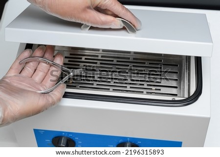 Hand with manicure and pedicure forceps after sterilization and disinfection from bacterial and viral infections in dry hot air sterilizer. Royalty-Free Stock Photo #2196315893