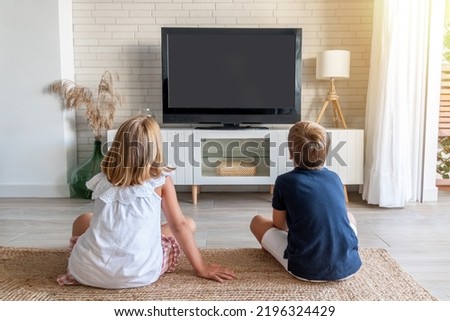 Two children sitting on the living room floor watching television. Mock up for inserting images in the tv Royalty-Free Stock Photo #2196324429