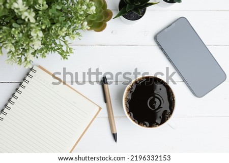 The desk office with a smartphone, blank notepad, coffee cup, and pen on a wood table. Flat lay top view copy space. Concept business technology.