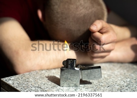 Gasoline lighter burns on table. Fire in background of sleeping guy. Party details. Smoking is harmful to health. Royalty-Free Stock Photo #2196337561