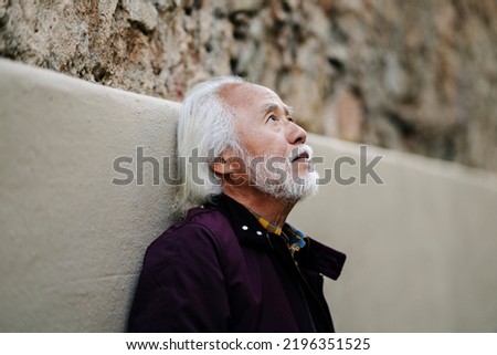 Portrait of an elderly Asian man in the city looking up, thoughtful. Royalty-Free Stock Photo #2196351525