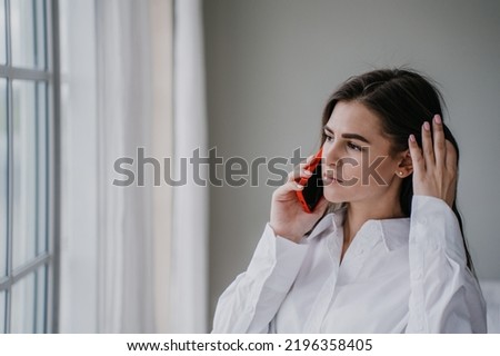 Frustrated brunette hispanic young woman talking by phone with husband, in troubles. Pretty caucasian girl at home using cell phone looking hopelessly at window. Upset housewife. Mockup sad girl. Royalty-Free Stock Photo #2196358405