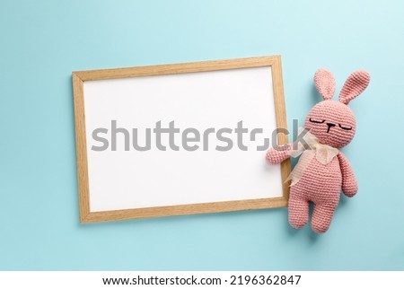 Blank white board with toy bunny on turquoise background, flat lay. Space for text
