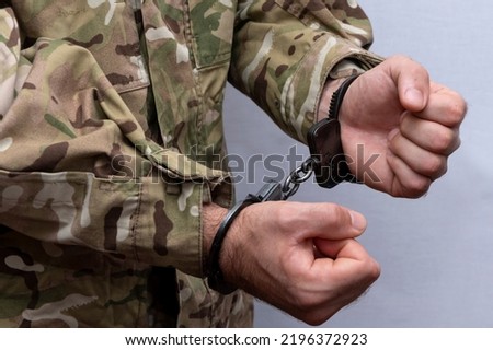 A soldier in a military camouflage uniform is handcuffed on a light background. Concept: a military tribunal over a criminal, an army court.
