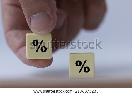 Hand is holding a piece of scrabble   with green percentage sign symbolising that the interest rates are neutral.