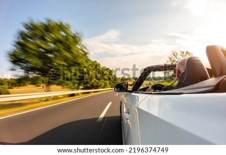 Adult man is driving with convertable car in sunny nature on a bright summer day. wide angle pursuit shot with high speed motion blur. Royalty-Free Stock Photo #2196374749