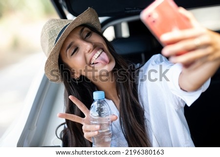 Shot of beautiful woman taking selfies with smartphone while drinking water sitting in the trunk of the car in the forest.