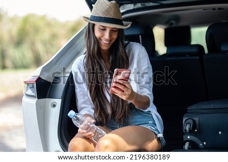 Shot of beautiful woman taking selfies with smartphone while drinking water sitting in the trunk of the car in the forest.
