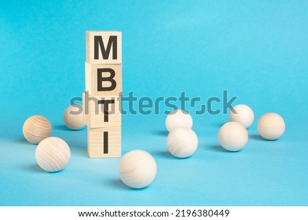a pyramid of wooden cubes with the word MBTI and wooden balls around on a bright blue background, copy space on the right