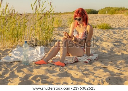 The woman was sunbathing and looking at the phone and looking at the sea, what are the children doing on the shore.