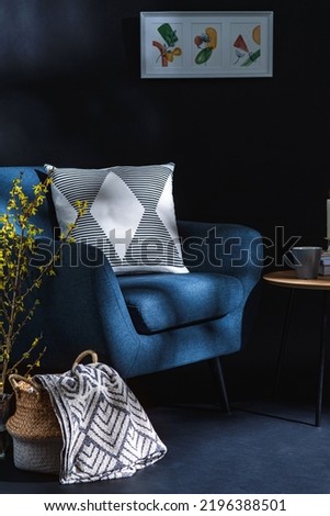 interior and home decor concept - close up of blue chair with pillow, blanket in wicker basket and tree branches in vase over black wall