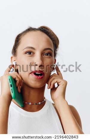 A woman listening to music and audio on wireless headphones and smiling with her teeth against a white background with a phone in her hands. Technology and lifestyle