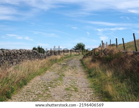 Narrow dirt lane running alongside dry stone walls with hillside meadow in calderdale west yorkshire near hebden bridge Royalty-Free Stock Photo #2196406569