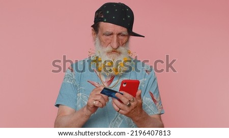 Sincere mature man customer using credit bank card and smartphone while transferring money, purchases online shopping, payment. Finance and internet. Senior grandfather alone on pink wall background