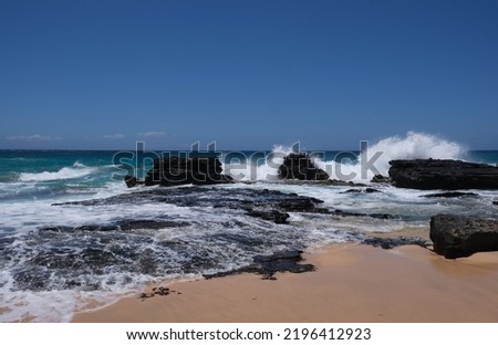 East Oahu Hawaii waves crashing over black lava rocks along the coastline.  Blue sky horizon over water against the Pacific Ocean.  White water created from waves and tidepools.