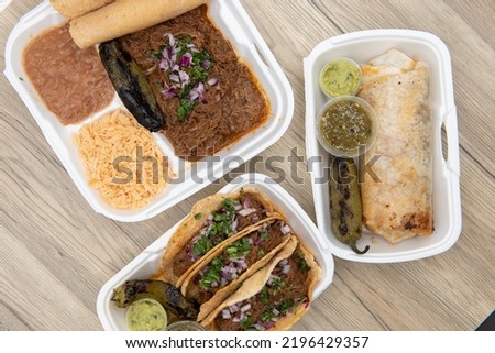 Overhead view of Mexican food feast on the table with choices of burrito, birria stew meat combo, or 3 tacos served with guacamole, salsa, and a grilled jalapeno.