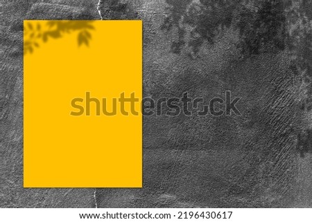 Empty yellow square poster mockup with light shadow on black concrete wall background. top view.