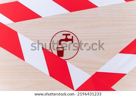 Protective tape covers wooden collector cabinet of water pipe in building. Cabinet door with water taps icon is sealed with barrier tape. Access to collector cabinet is blocked by striped tape