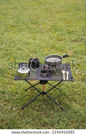 Picnic in nature at the table, tourist utensils for camping, equipment for cooking in the forest, gas burner, kettle with mug, frying pan. High quality photo