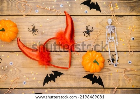 Women's accessories for a Halloween party. A flat headband with devil horns, pumpkin, skeleton, spiders and bats on a wooden background. A festive Halloween theme.
