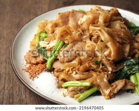 dish of PAD SEE EW, Thai stir-fried flat noodles with dark soy sauce served with chili flakes and sugar, on wooden table Royalty-Free Stock Photo #2196470405