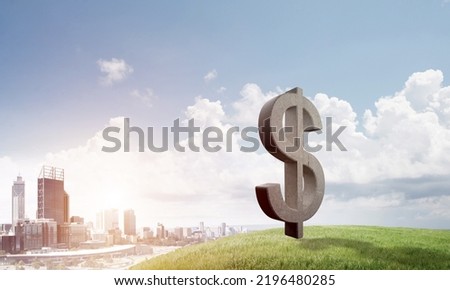 Stone dollar symbol outdoors on green hill as currency sign