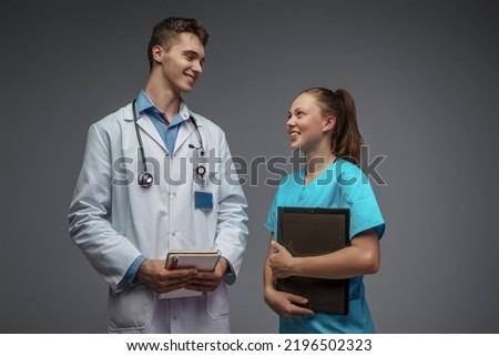 Photo of nurse with folder and doctor dressed in white labcoat looking each other.