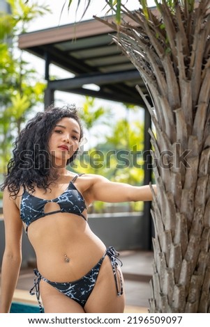 Young woman slim tanned body in bikini on Palm leavers ,positive redhead woman with clean skin and natural beauty standing behind tropical leaf, summer vacation skincare concept. bikini in nature