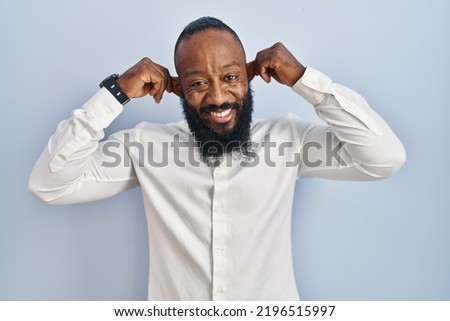 African american man standing over blue background smiling pulling ears with fingers, funny gesture. audition problem 