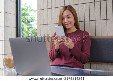 Portrait image of a young woman holding and using smart phone and laptop computer in cafe