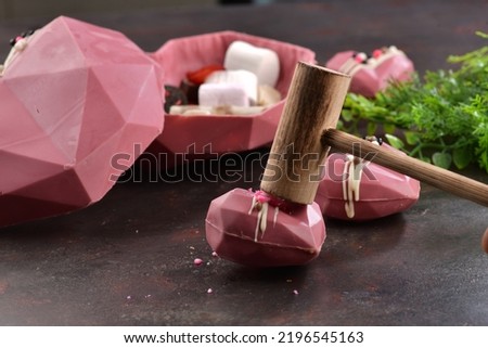 Pink chocolate with the shape of heart. Peanuts in the chocolate. Concept of love with Delicious heart shaped chocolate pictures. Chocolate with small wooden hammer. Chocolates on the brown background