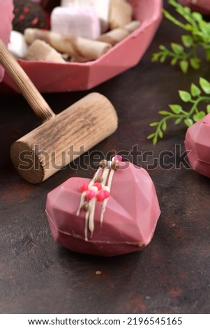 Pink chocolate with the shape of heart. Peanuts in the chocolate. Concept of love with Delicious heart shaped chocolate pictures. Chocolate with small wooden hammer. Chocolates on the brown background