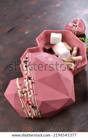 Pink chocolate with the shape of heart. Peanuts in the chocolate. Concept of love with Delicious heart shaped chocolate pictures. Selectively focused on chocolate. Chocolates on the brown background. 